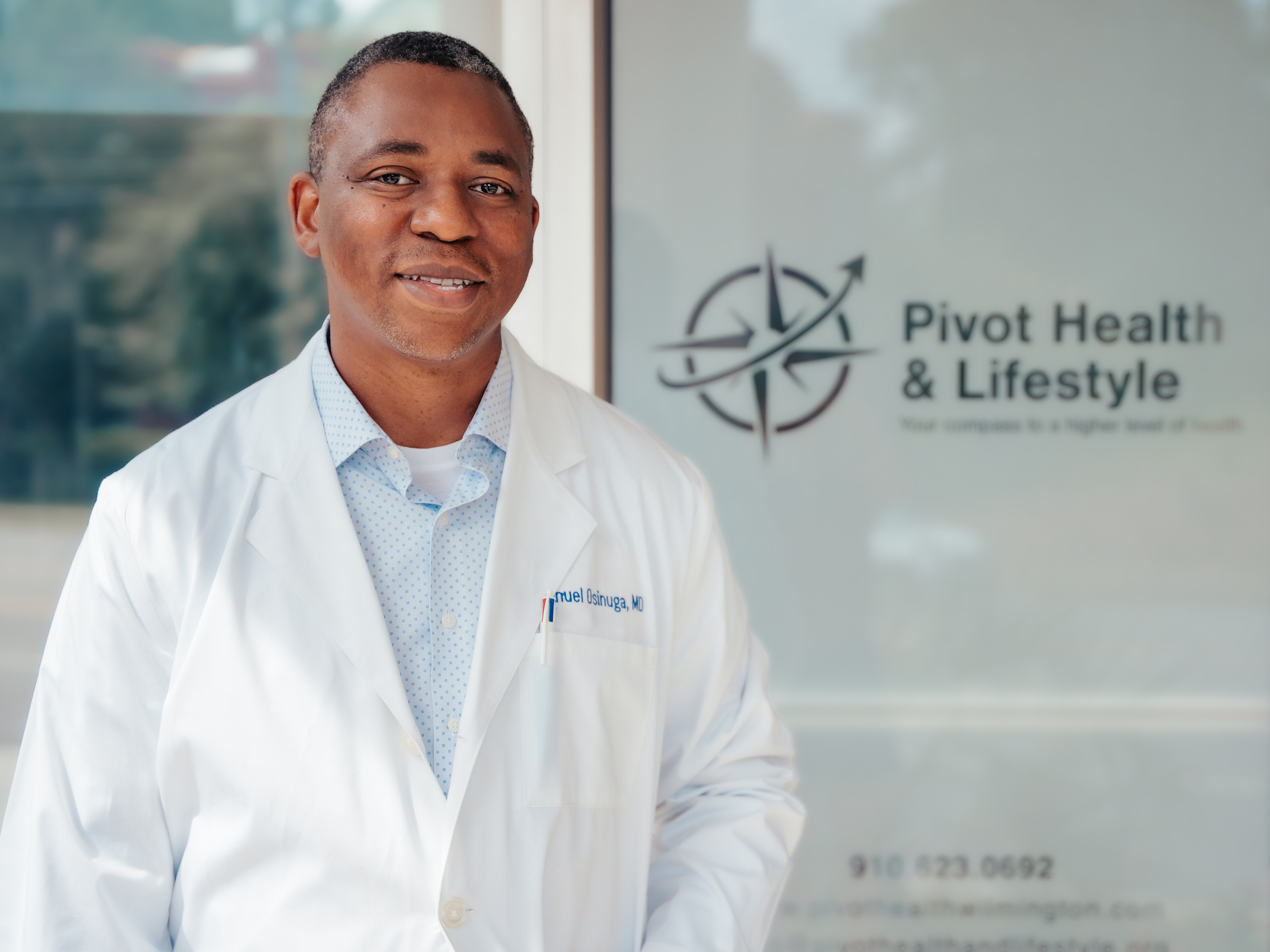 Dr. Emmanuel Osinuga in his white coat at the entrance to Pivot Health & Lifestyle