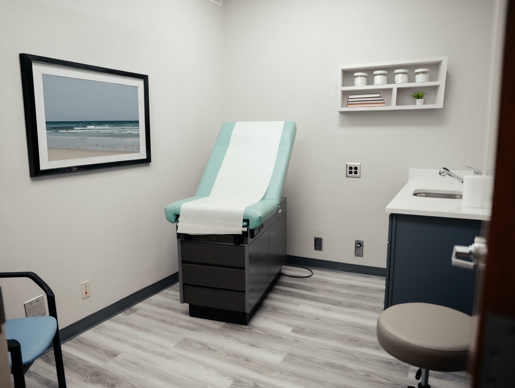An exam room at Pivot Health & Lifestyle, with a framed beach print and a wall shelf